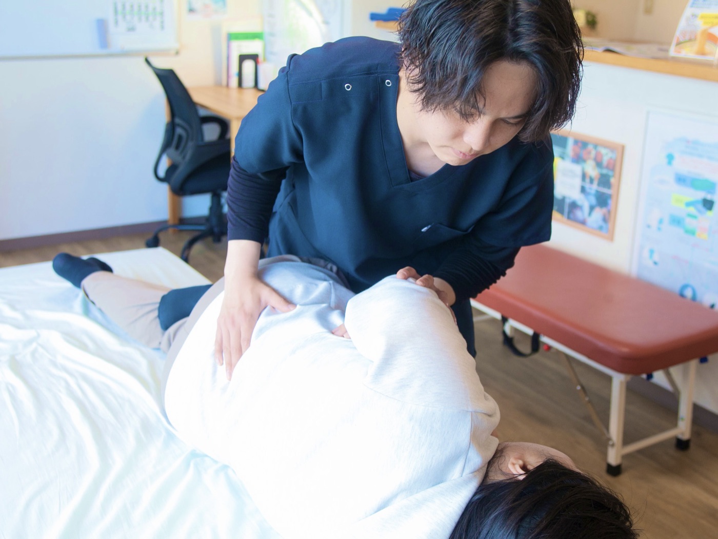 横向きに寝た女性の骨盤と肩に手を添えて施術している様子